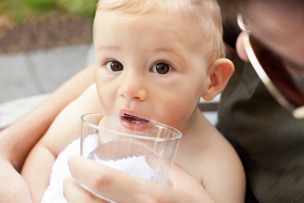 Father helping baby boy drink from cup