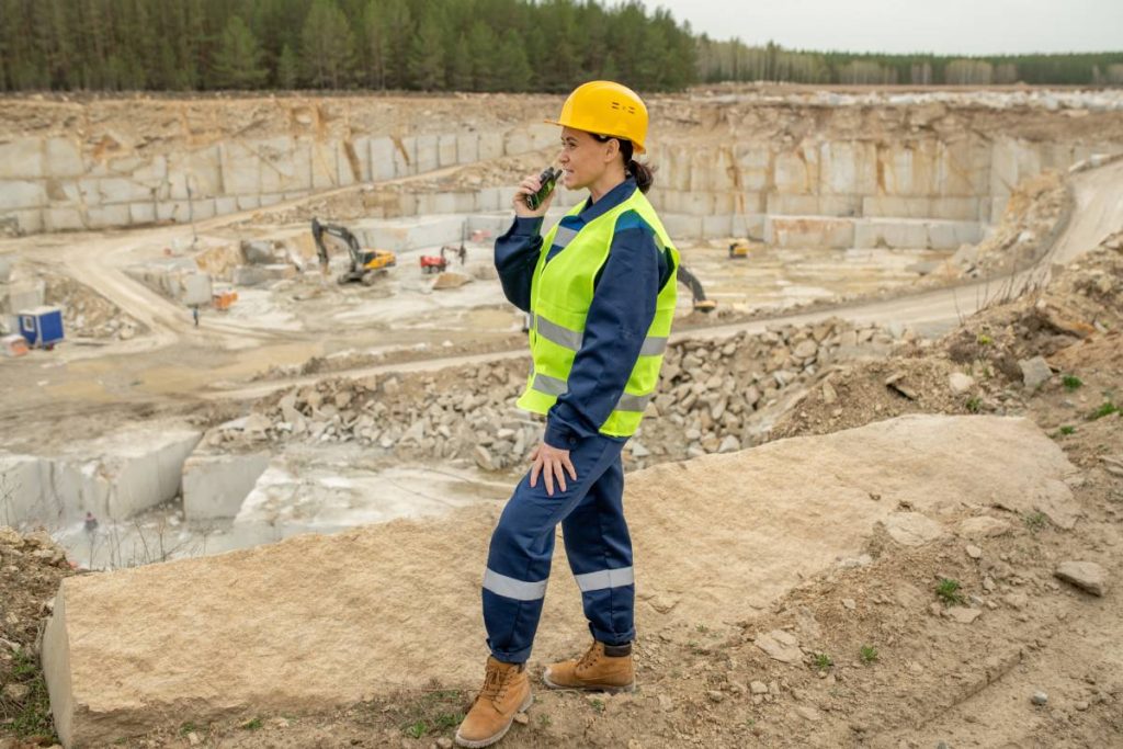 Female builder in uniform using walkie-talkie on construction site
