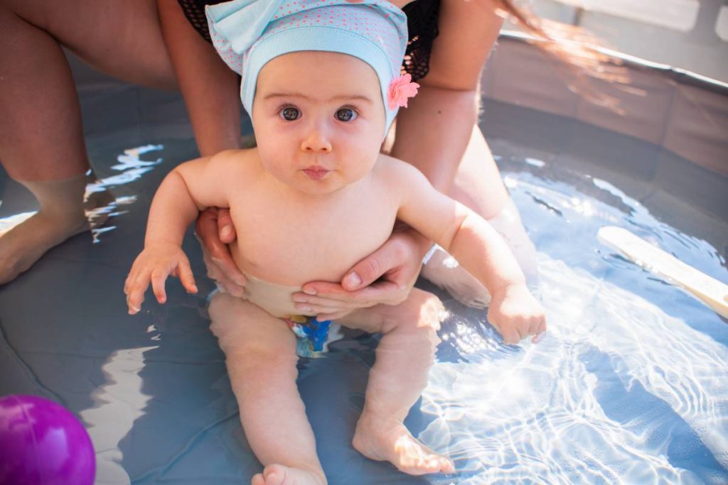 Mother holding baby girl first time in swimming pool. summer activities.