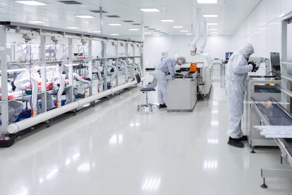 factory workers in white lab suits and black latex gloves, working with some modern equipment in a very clean room.