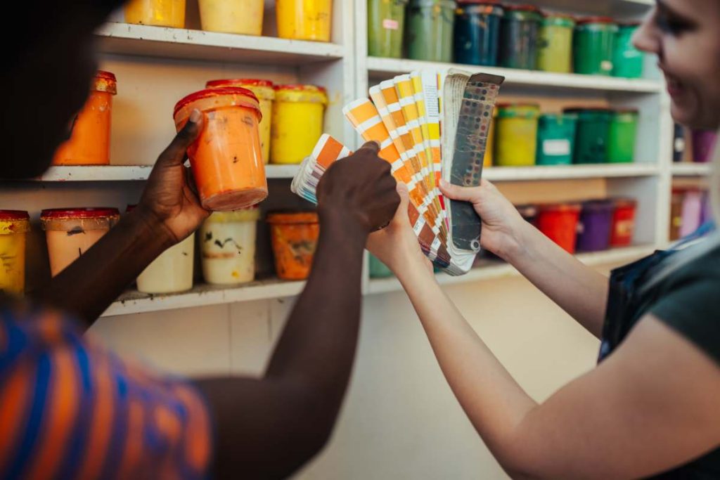 Cropped picture of multicultural graphic technology female workers' hands holding paint bucket and color swatch in printing workshop. Close up of silk screen printers choosing paint buckets for print.