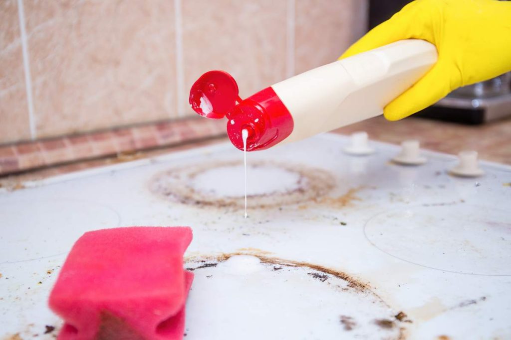 Man cleaning ceramic modern stove or hob with detergent agent. Hand in yellow gloves clean stove from burnt and grease dirt. Housework, professional cleaning service after tenants