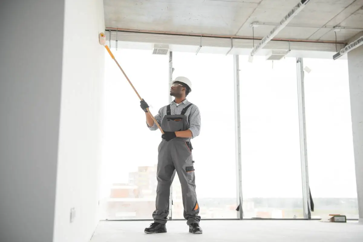 African man paints a white wall with a roller. Repair of the interior.
