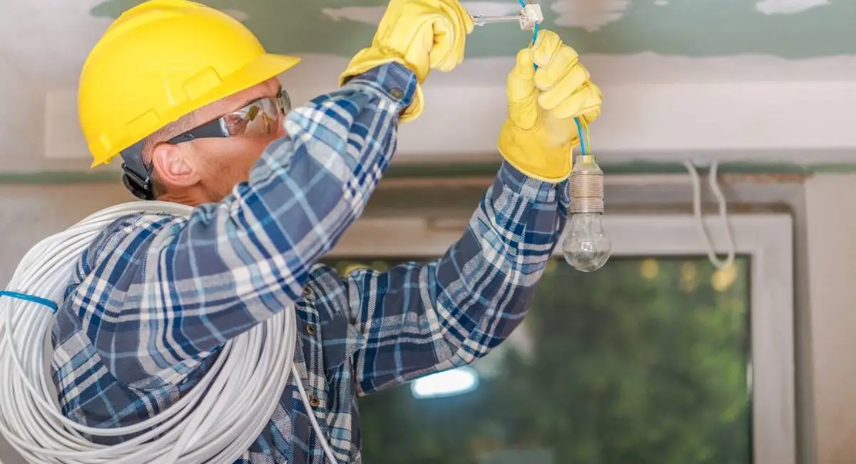 Caucasian Electrician in Yellow Safety Hard Hat at Work. Reinstallation of Residential Electrical System.
