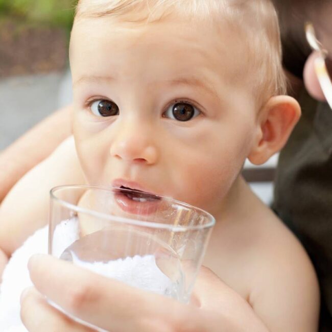 Father helping baby boy drink from cup