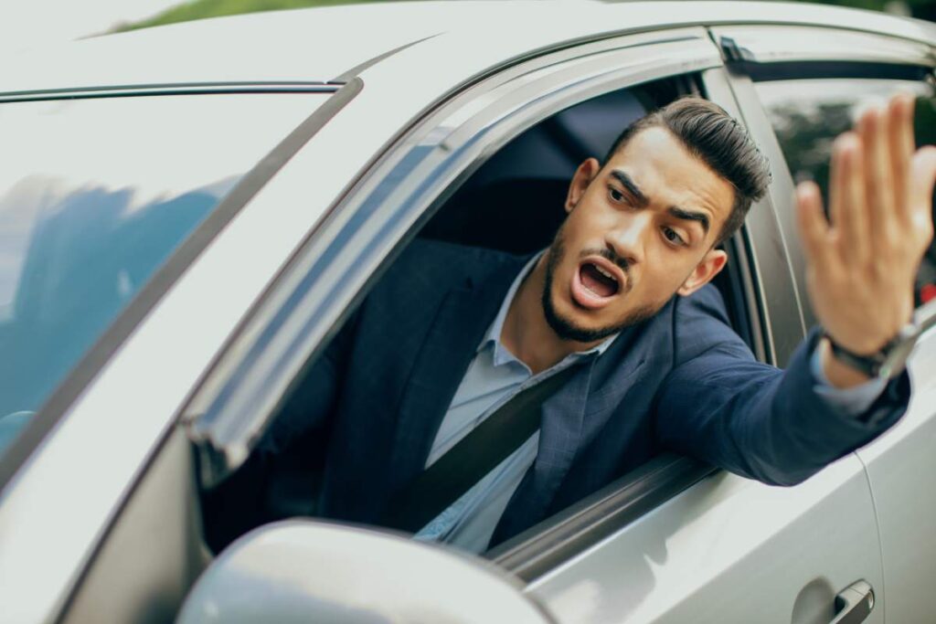 Furious middle-eastern businessman driving car, fighting with other drivers on road, emotional arab man getting late for business meeting or flight, stuck in traffic, yelling and gesturing