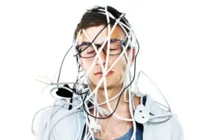 A man with glasses on tangled in a bunch of wires with a white background