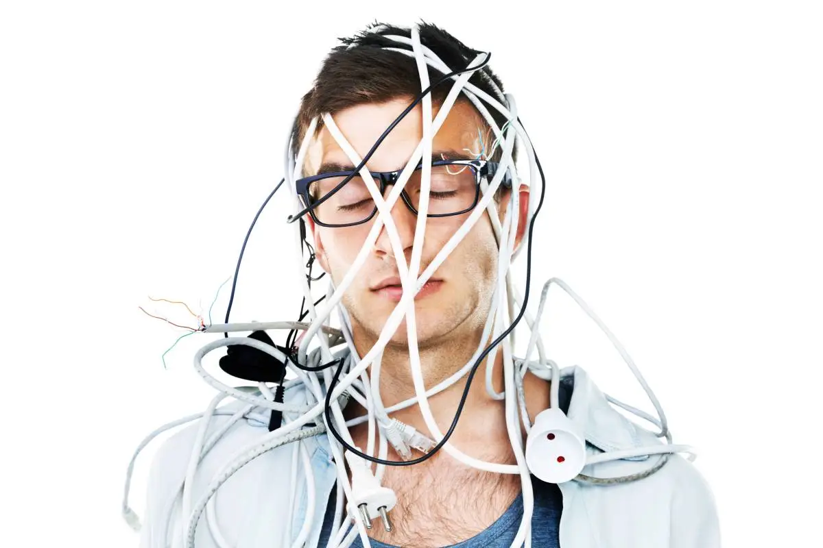 A man with glasses on tangled in a bunch of wires with a white background