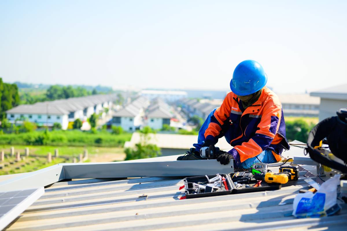 Male technician worker installing solar panels on rooftop of industrial plant, Engineer operating system at solar cell farm power plant, Renewable energy source for electricity and power, Solar energy concept