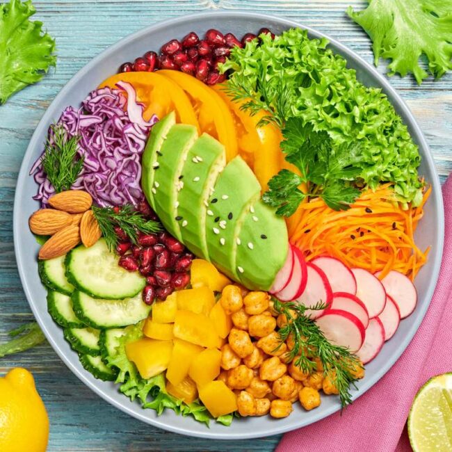 Buddha bowl salad with avocado, tomato, lettuce, cucumber, red cabbage, chickpeas, pomegranate. Paleo diet, healthy vegan and balanced food concept. Fresh rainbow mix green salad on wood, flat lay