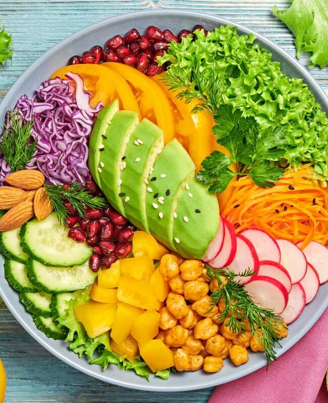 Buddha bowl salad with avocado, tomato, lettuce, cucumber, red cabbage, chickpeas, pomegranate. Paleo diet, healthy vegan and balanced food concept. Fresh rainbow mix green salad on wood, flat lay