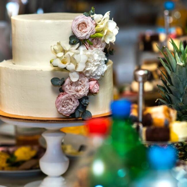 Tall sweet wedding cake decorated with live pink and white flowers on a table.