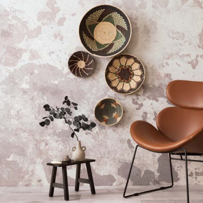 The stylish ethnic composition at living room interior with design brown armchair, colorful baskets, coffee table and elegant personal accessories. Grey concrete wall. Cozy apartment. Home decor.