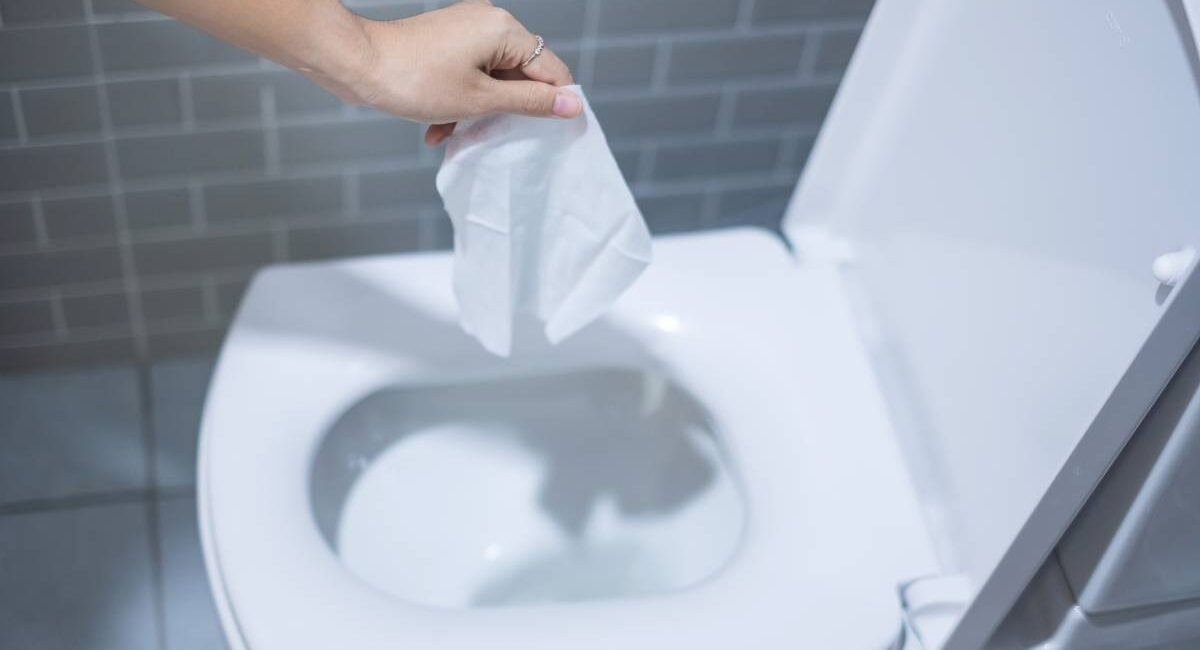 Woman hand throw paper towels in the toilet bowl. Cleaning, Lifestyle and personal hygiene concept